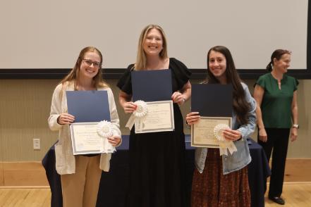 - Three Longwood graduates smile while holding certificates and award ribbons.
