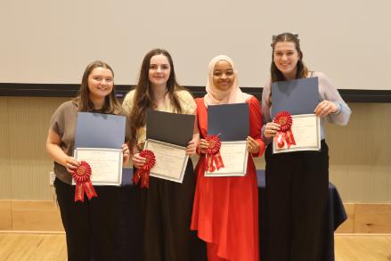 - Four Longwood graduates smile while holding certificates and second-place award ribbons.