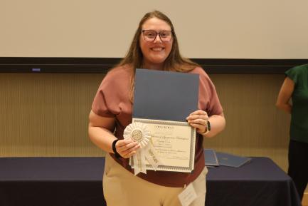 - A Longwood graduate smiles while holding a certificate and third-place award ribbon.