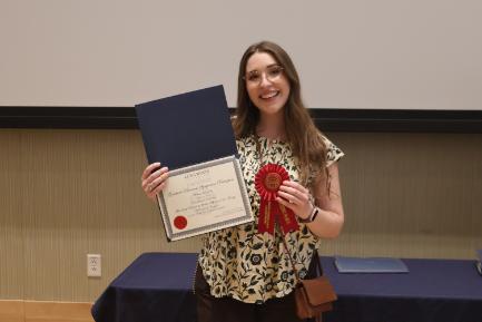 - A Longwood graduate smiles while holding a certificate and second-place award ribbon.