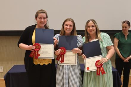 - Three Longwood graduates smile while holding certificates and second-place award ribbons.