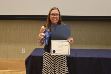 - A Longwood graduate smiles while holding a certificate and first-place award ribbon.