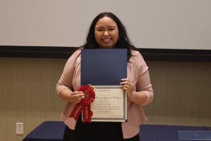 - A Longwood graduate smiles while holding a certificate and second-place award ribbon.