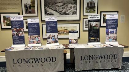 Education Immersion Day- photo fo a table of Longwood University Marketing Material for High School students - A display table at Longwood University features informational posters and framed images promoting the Office of Teacher Preparation, with materials outlining program benefits, requirements, and opportunities.