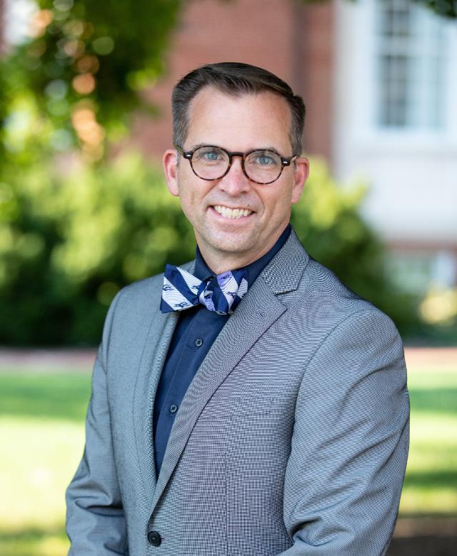 Vertical picture of Chris Kukk in a Lancer blue and white bow tie, blue shirt, and grey jacket