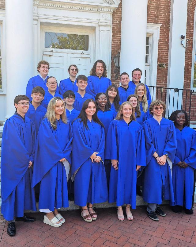 The 2024-2025 members of Honor & Conduct Board stand in front of Eason Hall - Group of students wearing blue robes stand together on the steps of a campus building. They are arranged in several rows in front of white columns and a brick façade. The students smile toward the camera during what appears to be a group portrait. A doorway and campus architecture form the background behind the gro