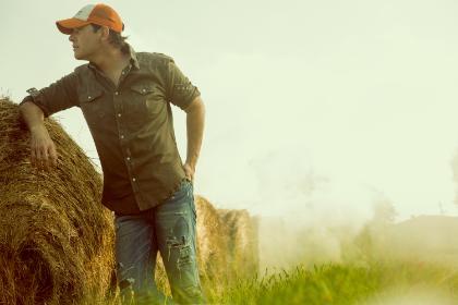 Rodney Atkins leaning against a round hay bale